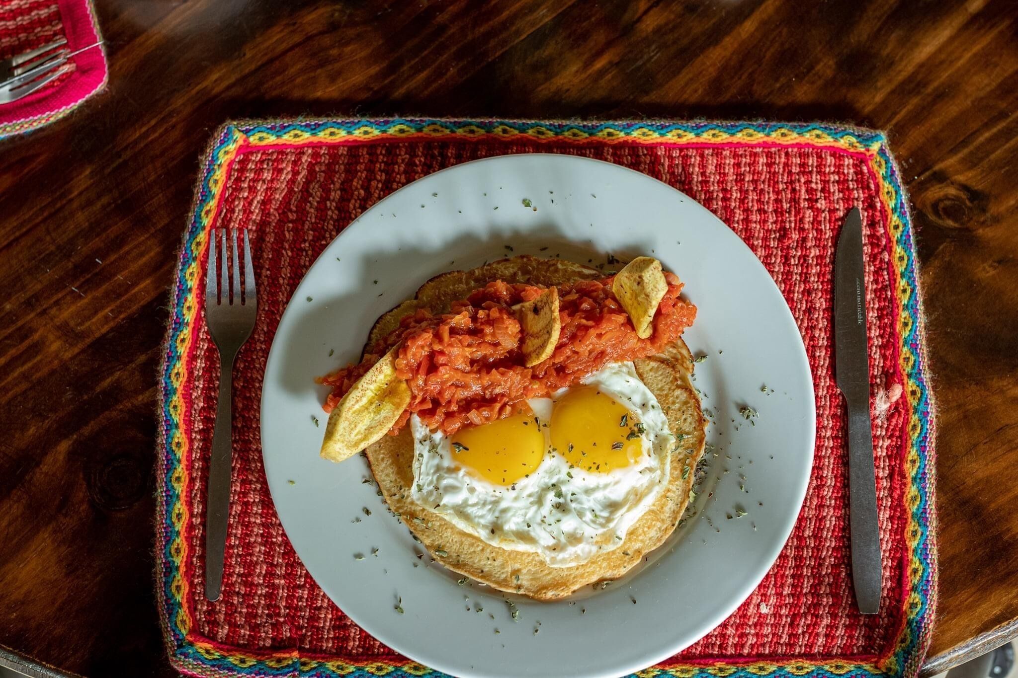 Een bord met eieren, tomaten en toast op een tafel met een kleurrijke placemat.