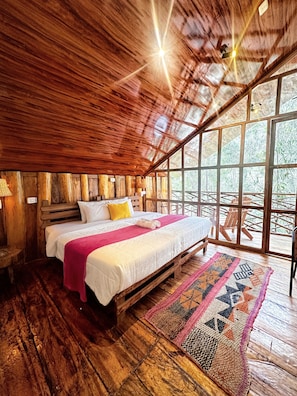 A wooden interior with a bed, a window, and a ceiling light. - Eco Quechua (Santa Teresa)