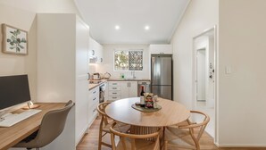 Una cocina moderna con armarios blancos, una mesa de comedor con sillas, un refrigerador y una computadora.