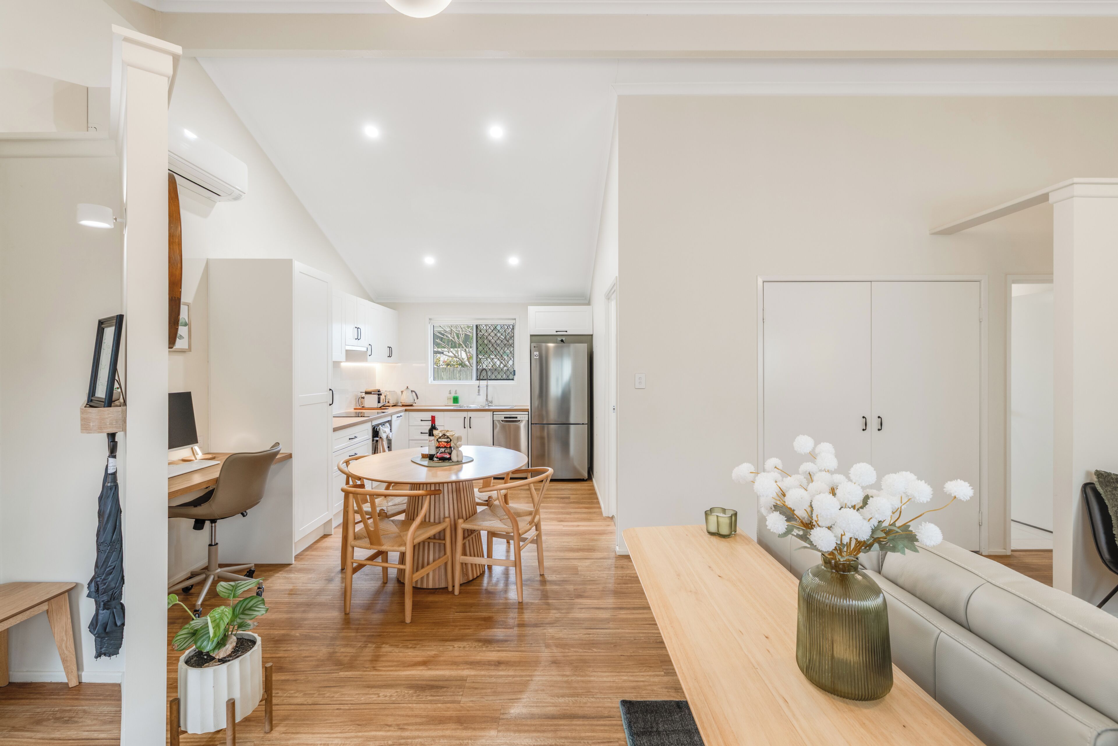 A modern kitchen with white cabinets, a dining area with a round table and chairs, and a living area with a sofa and a vase of flowers.