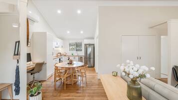 A modern kitchen with white cabinets, a dining area with a round table and chairs, and a living area with a sofa and a vase of flowers.