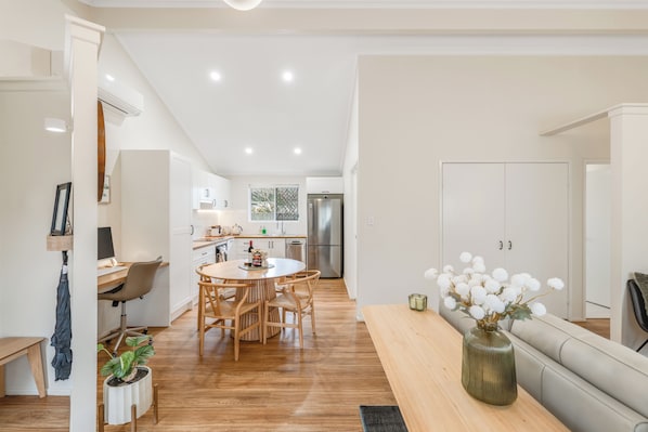 A modern kitchen with white cabinets, a dining area with a round table and chairs, and a living area with a sofa and a vase of flowers.