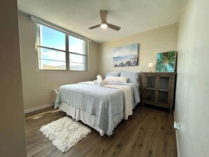 A bedroom with a bed, a ceiling fan, a window, and a painting on the wall. - Trade Winds | Family Vacation PH | Near Ferry (Ceiba)