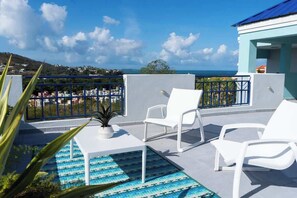 A rooftop terrace with a pool, white lounge chairs, and a view of the sea and distant buildings. - Trade Winds | Family Vacation PH | Near Ferry (Ceiba)