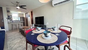 A dining area with a round table, chairs, and a television in the background. - Trade Winds | Family Vacation PH | Near Ferry (Ceiba)