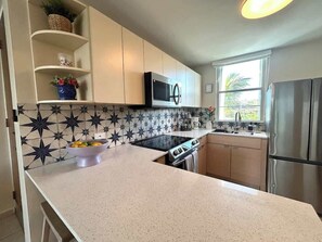 A kitchen with a microwave, stove, sink, and stainless steel refrigerator. - Trade Winds | Family Vacation PH | Near Ferry (Ceiba)