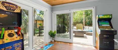 Habitación con juegos de arcade, puerta corredera de vidrio que da a un patio exterior y vistas al exterior.