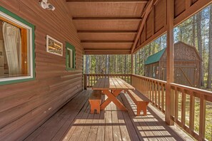 En stuga byggd av trä med en inglasad veranda, ett picknickbord och utsikt över skogen.