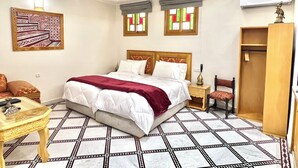 Una habitación de hotel con una cama grande, un armario de madera, una mesita pequeña y una silla.