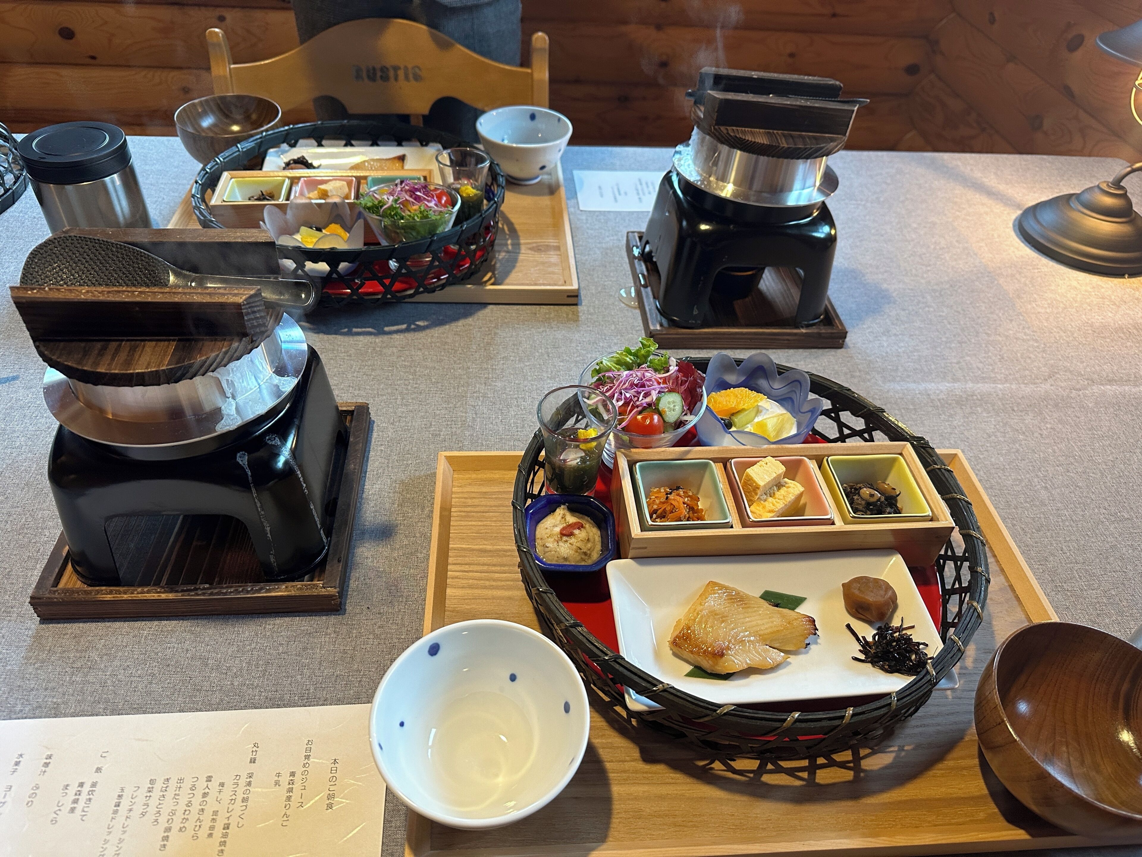 Une table à manger avec différents plats, notamment une salade, du pain et un plat de poisson, ainsi qu’une théière et des tasses.