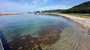 A coastal landscape with a clear sky, calm water, and a sandy beach.