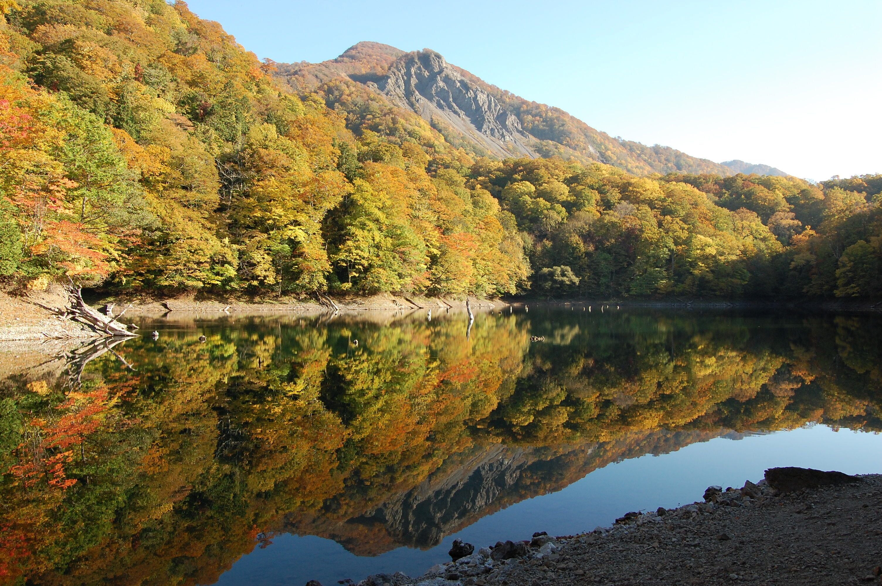A calm lake reflecting the surrounding autumn foliage and mountains.