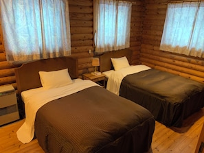 Una habitación de cabaña de troncos con dos camas, paredes de madera y una ventana con cortinas.