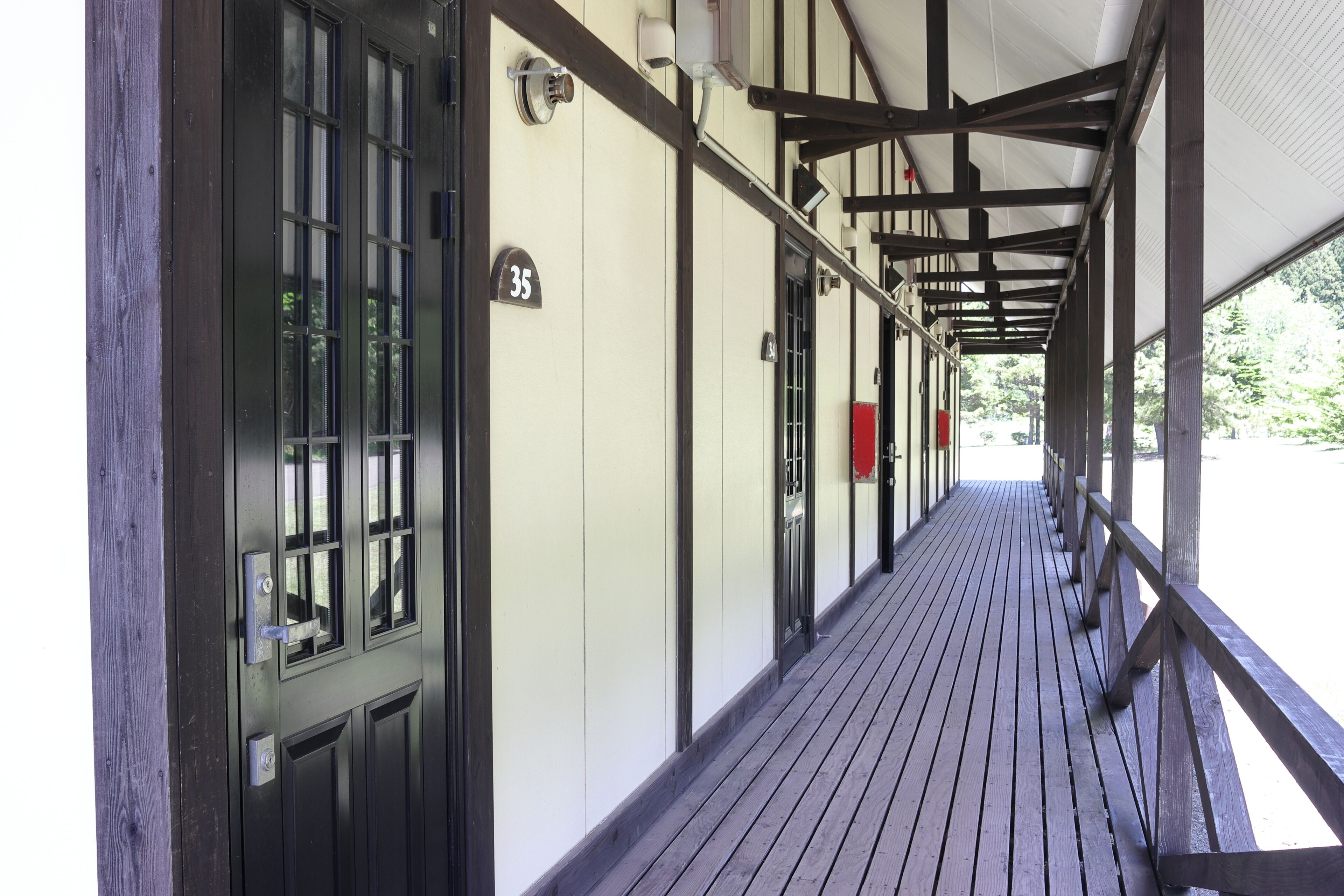 Un pasillo cubierto con piso de madera, barandales de metal y puertas con números que indican habitaciones o unidades.