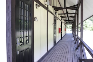 Un pasillo cubierto con piso de madera, barandales de metal y puertas con números que indican habitaciones o unidades.