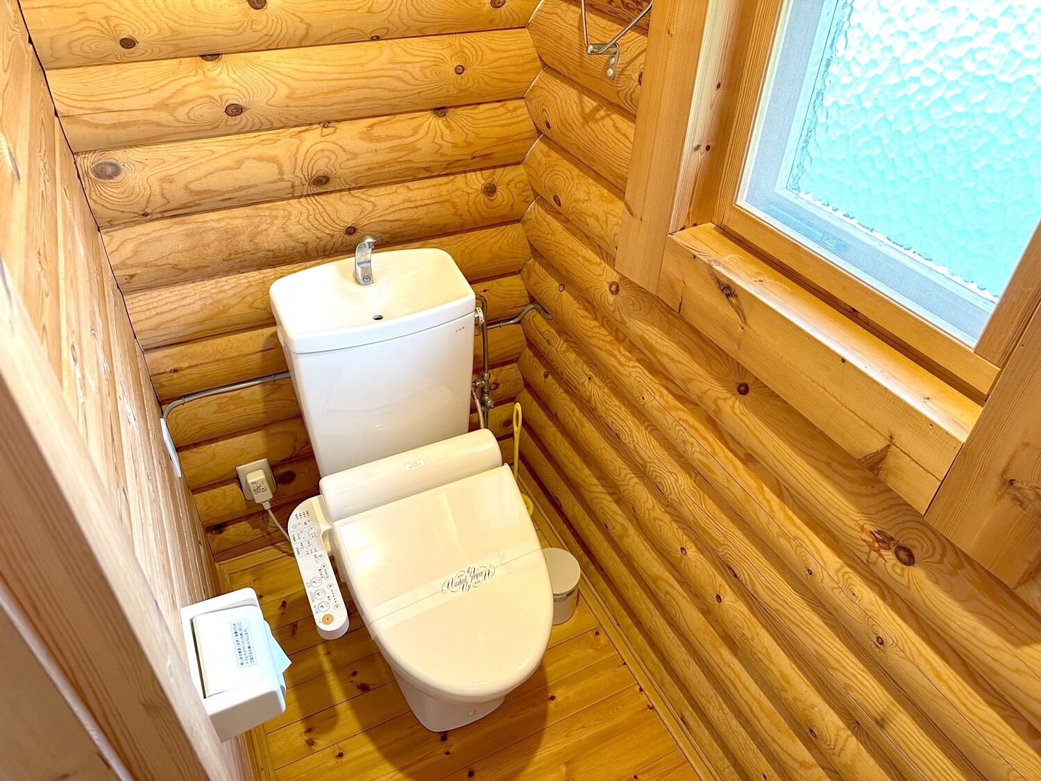 A compact wooden cabin bathroom with a toilet, a bidet, and a window.