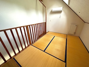 Una habitación con esteras de tatami, barandilla de madera, radiador y aire acondicionado de pared.