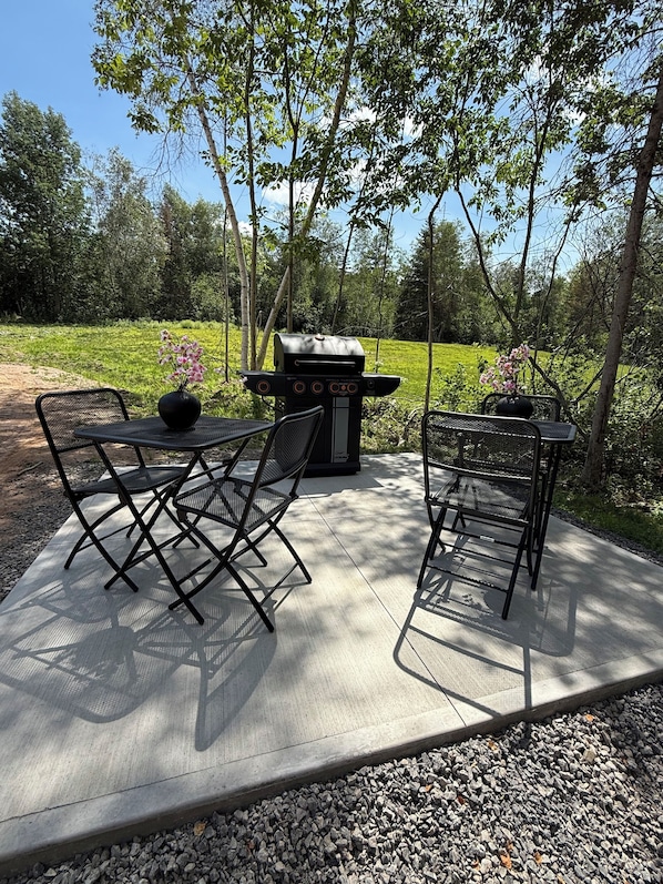 An outdoor patio with a grill, two chairs, and a table.