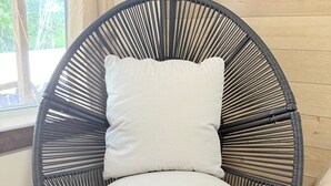 A round, black wicker chair with a white cushion, positioned against a wooden wall with a window. - Sakura Valley Studio Suite #7 / Private Entrance in beautiful Annapolis Valley (North Alton)