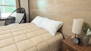 A bedroom with a bed, a nightstand with a lamp, a chair, and a window with curtains. - Sakura Valley Studio Suite #7 / Private Entrance in beautiful Annapolis Valley (North Alton)