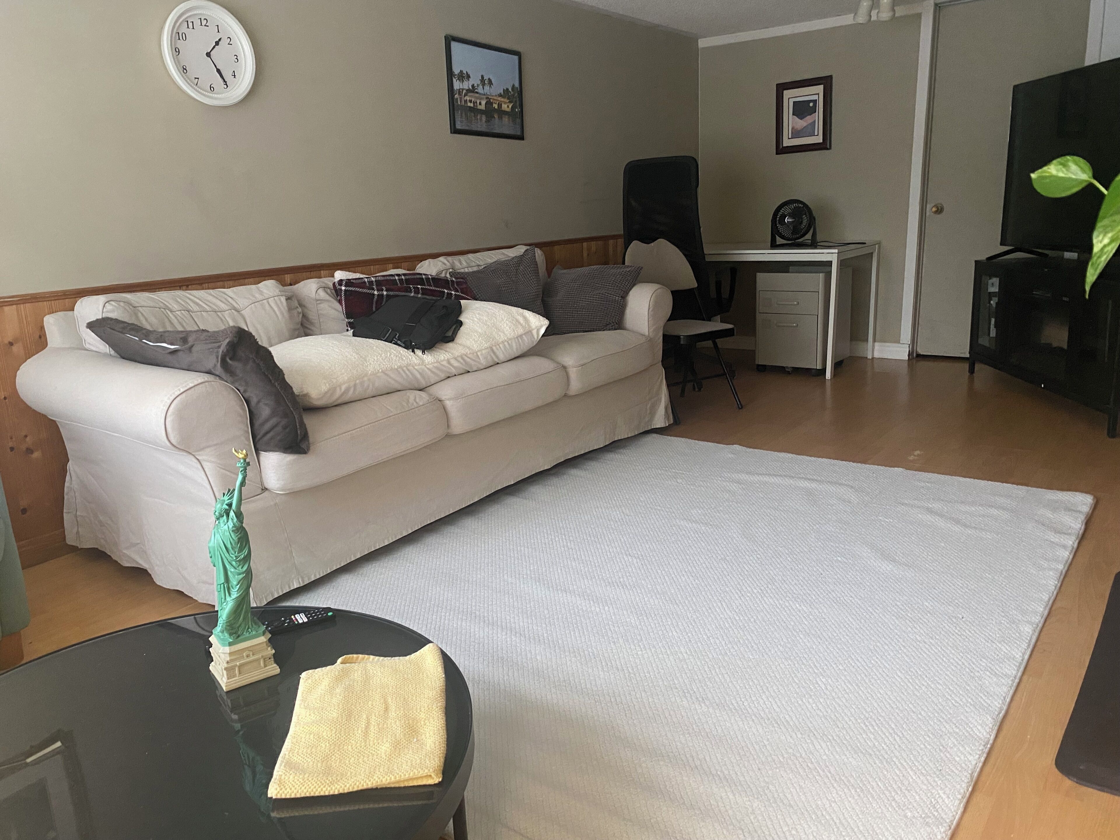 A living room with a sofa, a small table with a statue, a clock, and a TV.