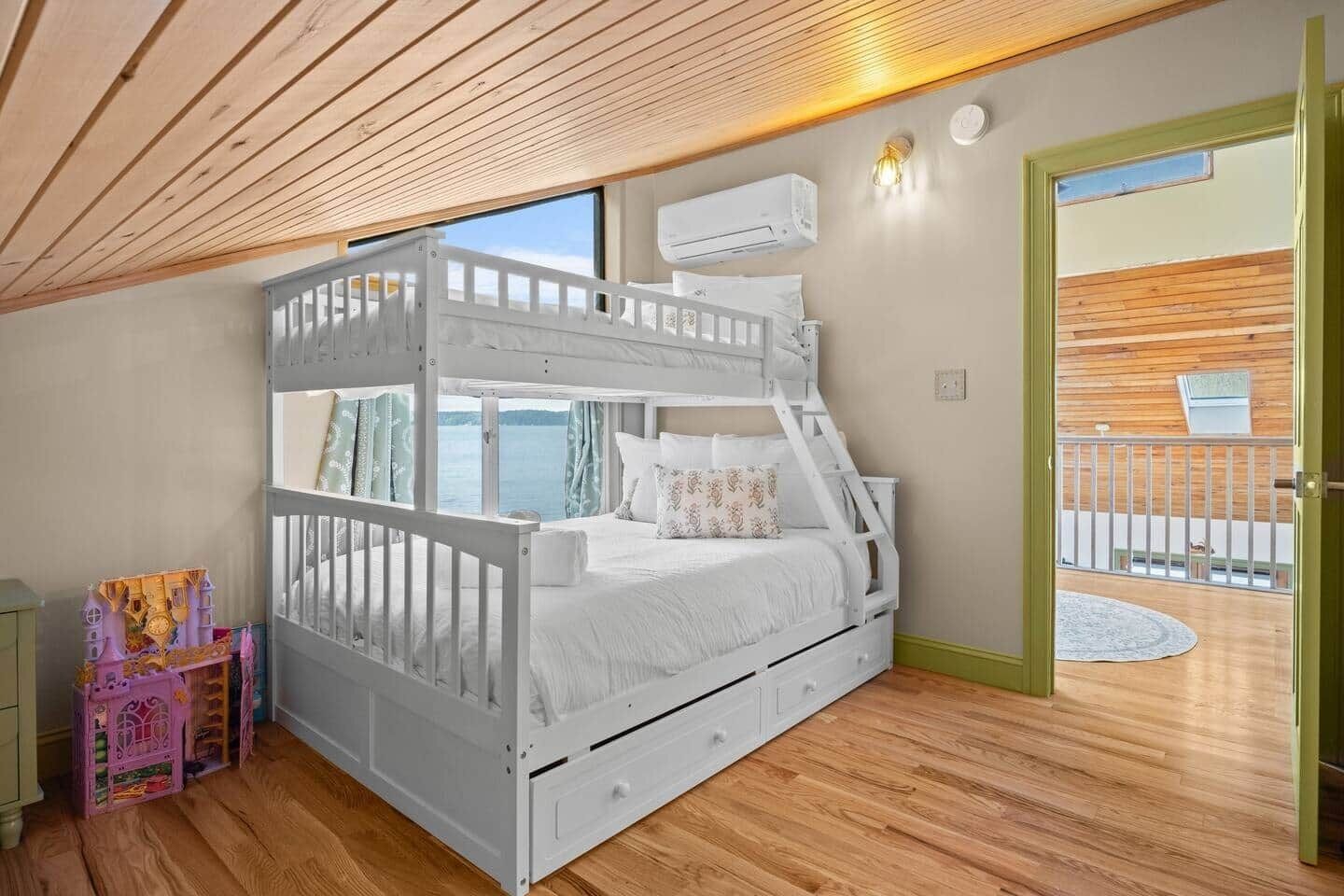 A bunk bed with a view of the water, a small table with a chair, and a door to an outdoor balcony.