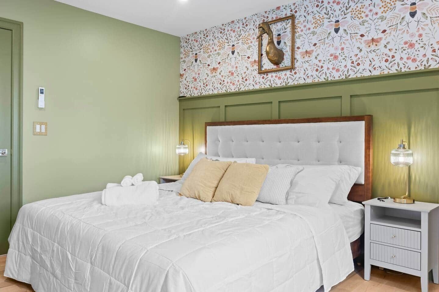 A hotel room with a large bed, two bedside tables, and a floral wallpaper design.