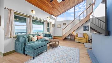 A spacious living area with a large window, a wooden ceiling, a staircase, and a sofa.