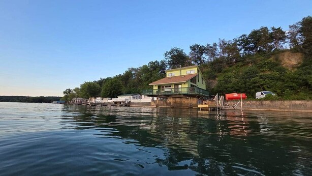 A waterfront property with a multi-story building, a dock, and a boat. - Long Point Lake House - Phil's Place (Ledyard)