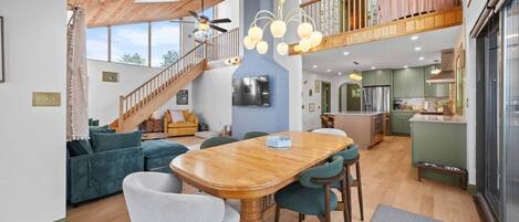 Un'ampia zona giorno con un tavolo da pranzo in legno, divani blu e una scala che conduce a un piano superiore.