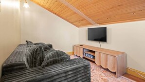 A room with a bed, a flat-screen TV mounted on the wall, and a wooden entertainment unit. - Long Point Lake House - Phil's Place (Ledyard)