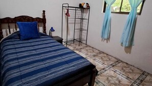 Een slaapkamer met een bed, een raam met gordijnen, een metalen rek en een wanddecoratie.