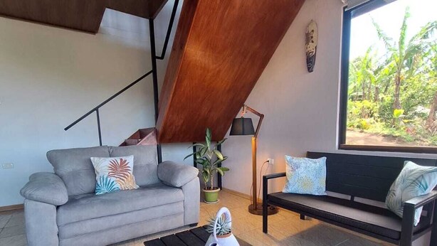 A modern living room with a sofa, a coffee table, and a bench. There is a window with a view of greenery outside. - Cecropia Paradise Monteverde (Santa Elena, Monteverde)