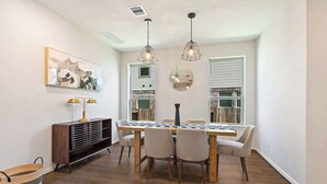 Un comedor con mesa de madera, sillas, luces colgantes, un espejo en la pared y un adorno sobre la mesa.