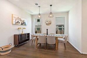 A dining area with a wooden table, chairs, pendant lights, a wall-mounted mirror, and a decorative piece above the table. - Luxury 4BR 3BA - Peaceful Forest Retreat (Willis)