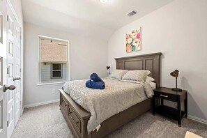 A bedroom with a bed, a nightstand, a window with blinds, and a door. - Luxury 4BR 3BA - Peaceful Forest Retreat (Willis)