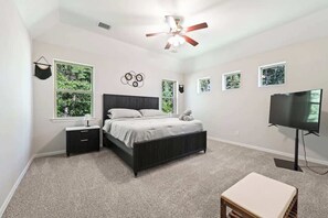 Un dormitorio con cama, televisor, ventilador de techo y ventanas.