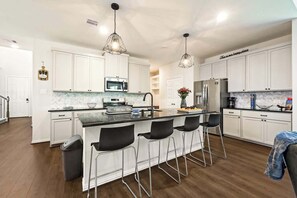 Una cocina moderna con gabinetes blancos, electrodomésticos de acero inoxidable y taburetes de bar.