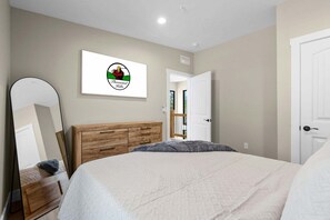 Een slaapkamer met een bed, een houten dressoir, een spiegel en een deur.