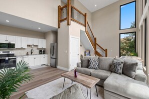 A modern kitchen with white cabinets, stainless steel appliances, and a wooden staircase leading to an upper level.