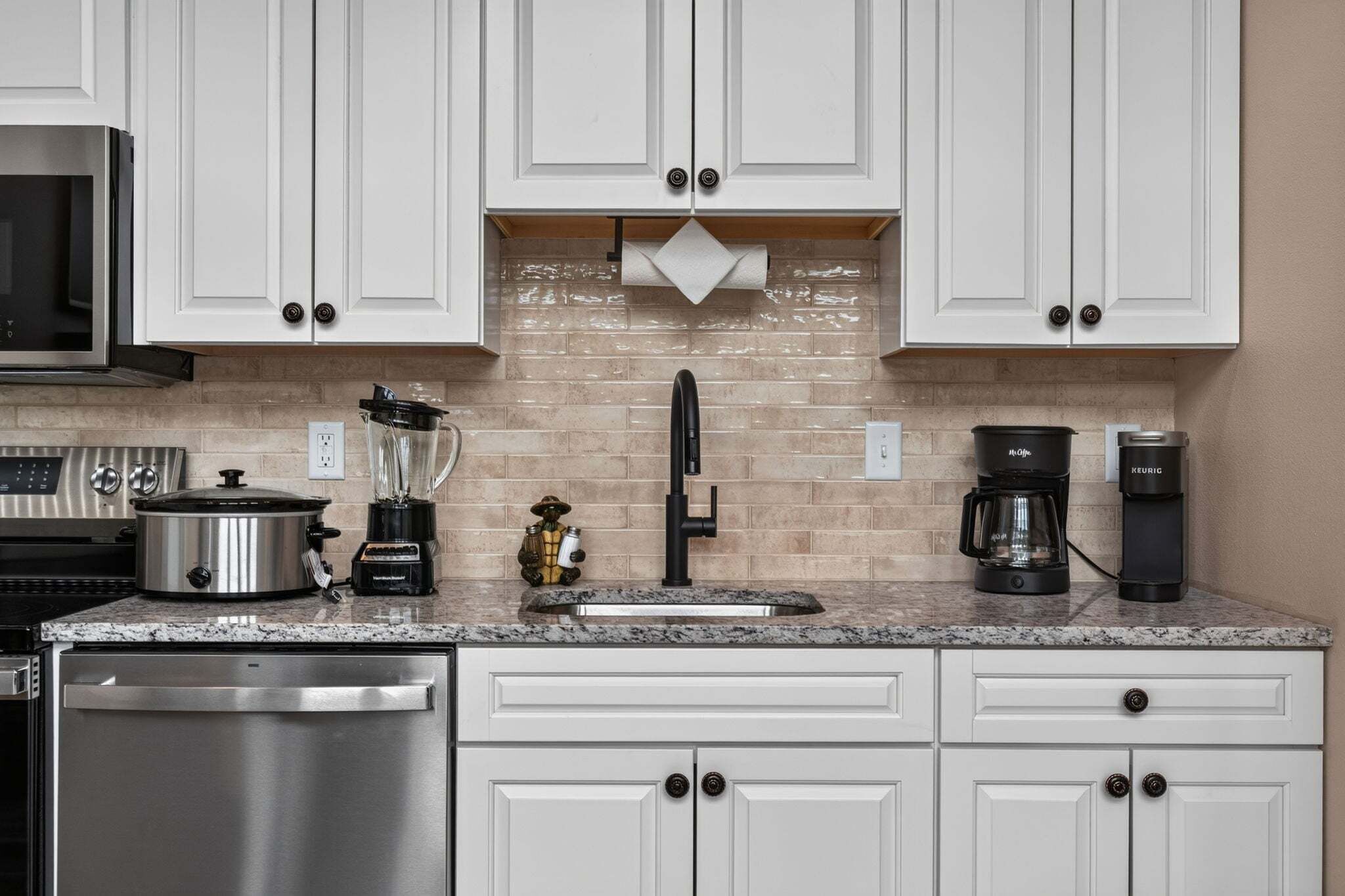 A modern kitchen with white cabinetry, a stainless steel dishwasher, a coffee maker, and a blender.