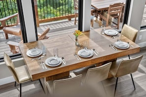 A dining table set for four with chairs, a vase with flowers, and a view of the outdoors.