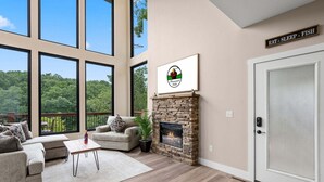 Amplia sala de estar con chimenea de piedra, ventanas grandes y una zona de estar acogedora.