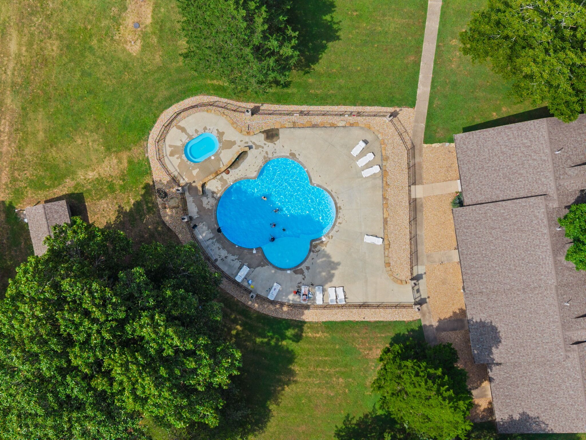 Vue aérienne d’une propriété résidentielle dotée d’une piscine, d’un jacuzzi séparé et d’un espace patio aménagé avec des chaises longues.