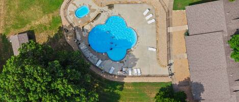 Vue aérienne d’une propriété résidentielle dotée d’une piscine, d’un jacuzzi séparé et d’un espace patio aménagé avec des chaises longues.