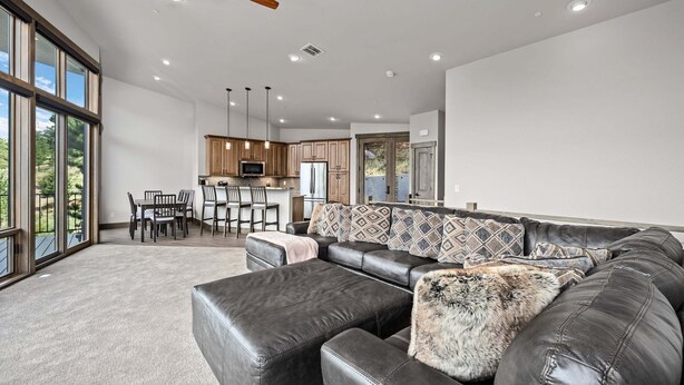 A spacious living area with a leather sofa, a dining table with chairs, and a kitchen in the background. - Aspen Trail Retreat - Breathtaking Mountain Views! (Estes Park)