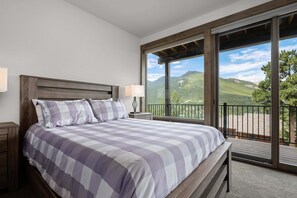 Ein Schlafzimmer mit einem großen Bett, zwei Nachttischlampen und Blick auf eine gebirgige Landschaft durch einen Balkon.