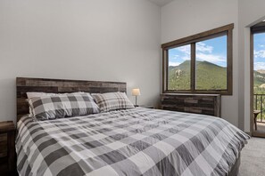 A bedroom with a large bed, a nightstand, a dresser, and a window with a mountain view. - Aspen Trail Retreat - Breathtaking Mountain Views! (Estes Park)
