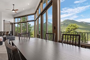 Ein geräumiges Zimmer mit einem großen Esstisch, Stühlen und Blick auf eine Berglandschaft durch große Fenster.