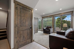 A spacious living area with a large sliding door, a leather sofa, and a view of a mountainous landscape through large windows. - Aspen Trail Retreat - Breathtaking Mountain Views! (Estes Park)